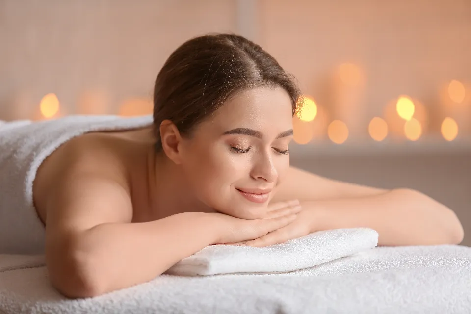 Eine Frau liegt entspannt auf einer Massageliege, im Hintergrund brennen Kerzen